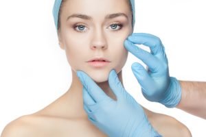 Plastic surgery concept. Doctor hands in gloves touching woman face